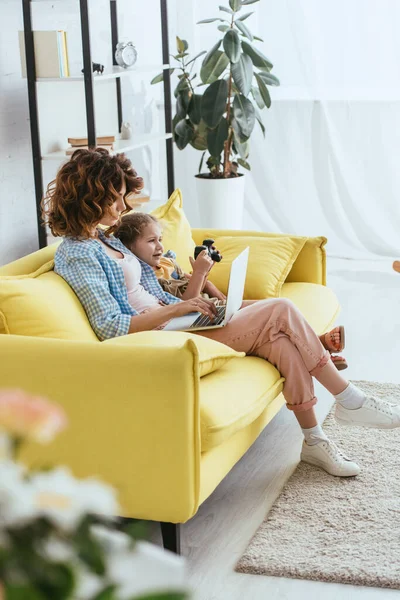 KYIV, UKRAINE - JUNE 19, 2020: selective focus of nanny working on laptop near cute child playing video game — Stock Photo