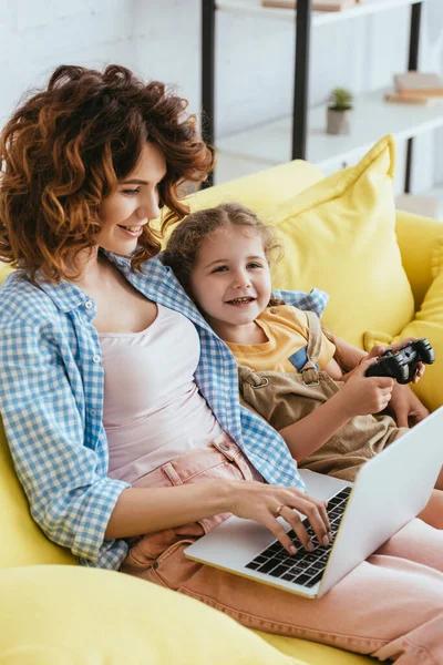 KYIV, UKRAINE - JUNE 19, 2020: smiling child holding joystick near young babysitter working on laptop — Stock Photo