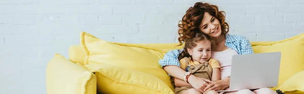 Horizontales Bild von lächelndem Babysitter und Kind, das auf dem Sofa sitzt und Laptop benutzt — Stockfoto