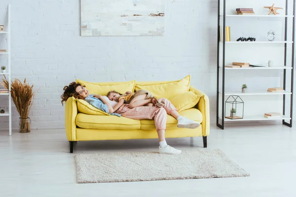 Glückliche Kindermädchen und entzückendes Kind lächeln in die Kamera, während sie zu Hause auf dem Sofa liegen — Stockfoto