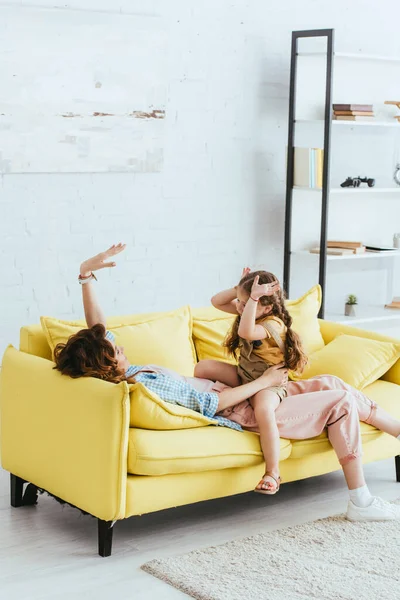 Kind sitzt auf jungem Kindermädchen und hat Spaß auf Sofa im Wohnzimmer — Stockfoto