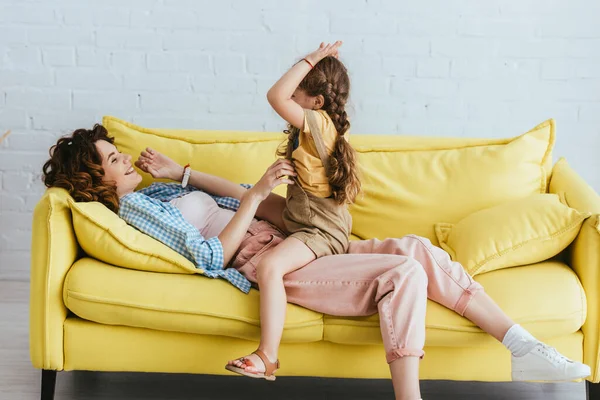 Kid sitting on cheerful babysitter while having fun on yellow sofa — Stock Photo