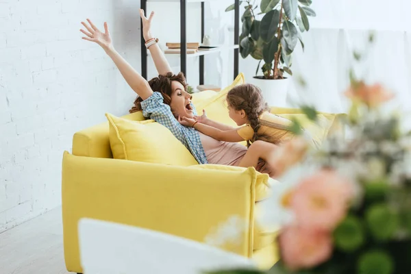 Selective focus of child tickling laughing nanny while having fun on sofa — Stock Photo