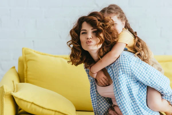 Young nanny making duck face while piggybacking kid at home — Stock Photo