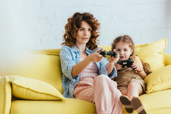 KYIV, UKRAINE - JUNE 19, 2020: focused nanny and cute child playing video game with joysticks — Stock Photo