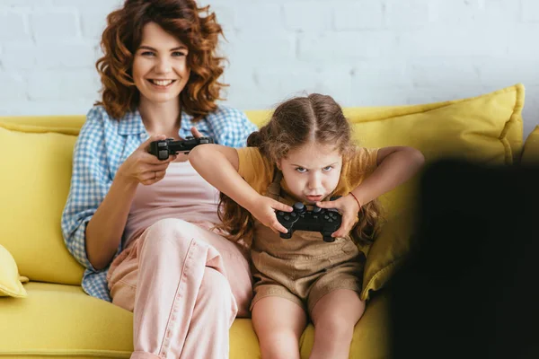 KIEW, UKRAINE - 19. JUNI 2020: Selektiver Fokus lächelnder Babysitter und konzentrierter Kinder, die Videospiele mit Joysticks spielen — Stockfoto