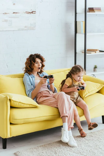 KYIV, UKRAINE - 19 JUIN 2020 : nounou excitée et enfant concentré jouant à un jeu vidéo avec des joysticks — Photo de stock