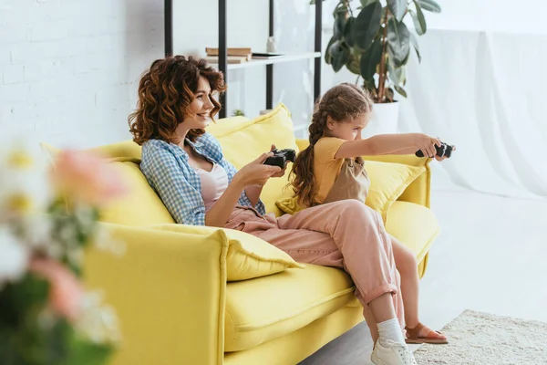 KIEW, UKRAINE - 19. JUNI 2020: Selektiver Fokus lächelnder Babysitter und Kind beim Videospiel auf gelbem Sofa — Stockfoto