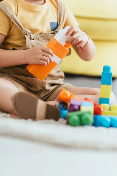 Vista parcial del niño sentado en el suelo y jugando con bloques de construcción multicolores, enfoque selectivo - foto de stock