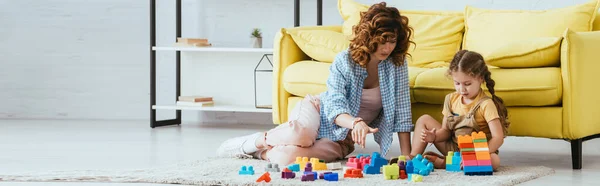 Concepto horizontal de niñera y lindo niño jugando con bloques de construcción multicolores en el suelo - foto de stock