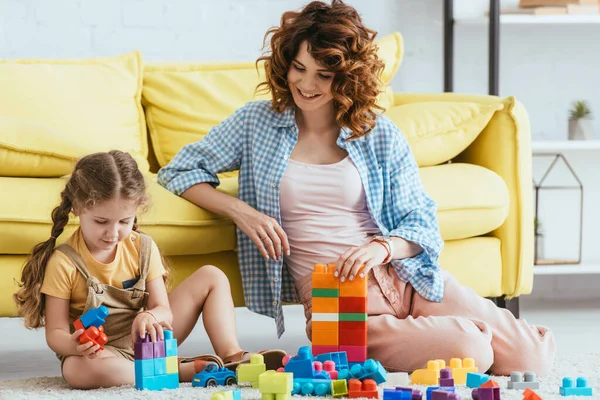 Bambinaia sorridente e adorabile bambino che gioca con mattoni multicolori sul pavimento — Foto stock