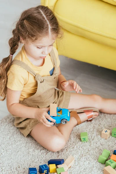 Vue grand angle de l'adorable enfant assis sur le sol et jouer avec la voiture jouet et les blocs de bois multicolores — Photo de stock