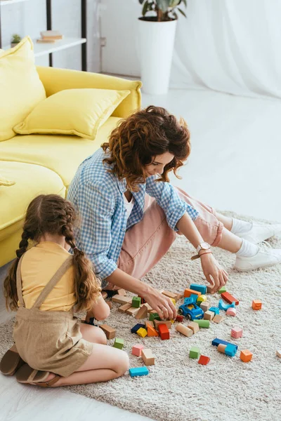 Високий кут зору дитини з нянею, що грає з різнокольоровими кубиками на підлозі — стокове фото