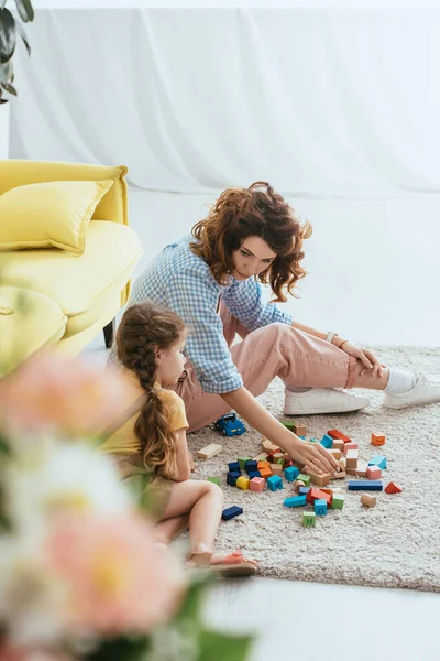 Enfoque selectivo de la niñera y el niño jugando con bloques multicolores en el suelo - foto de stock
