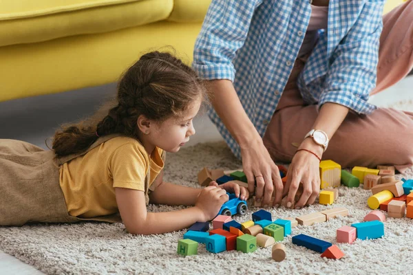 Vista recortada de la niñera y el niño jugando con bloques multicolores de piso - foto de stock