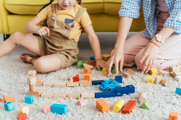 Vista parcial del niño y la enfermera jugando con bloques multicolores y coche de juguete en el suelo - foto de stock