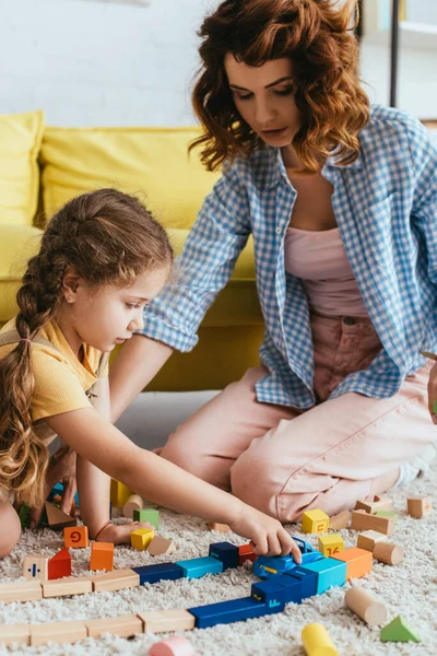 Bela babá e adorável criança brincando com blocos multicoloridos no chão — Fotografia de Stock