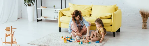 Горизонтальне зображення няні та дитини, що грає з різнокольоровими блоками на підлозі — стокове фото