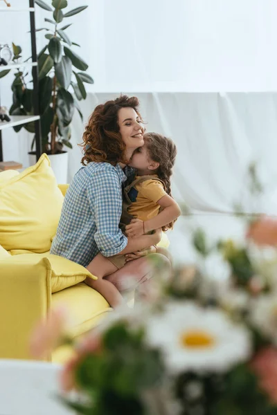 Избирательный фокус счастливой няни, обнимающей очаровательного ребенка, сидя на желтом диване — стоковое фото