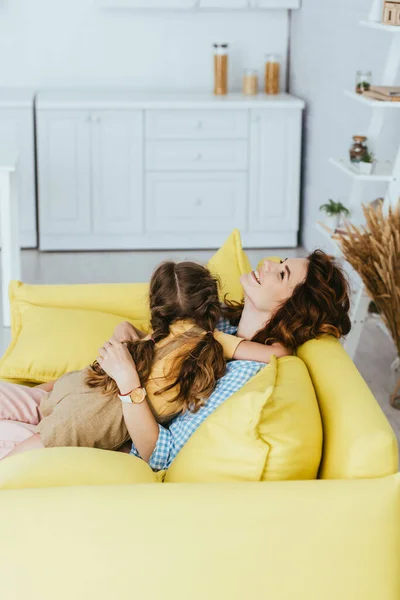 Счастливая няня обнимает ребенка, сидя на диване на кухне — стоковое фото