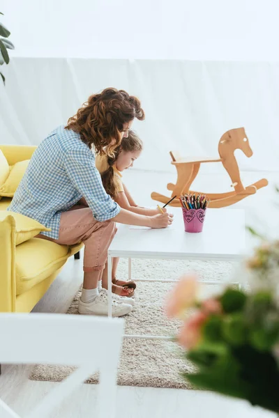 Selektiver Fokus von Babysitter und Kinderzeichnung mit Bleistiften in der Nähe von Schaukelpferden — Stockfoto