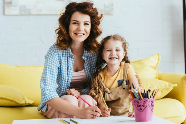 Happy nanny and kid smiling at camera while drawing together — Stock Photo