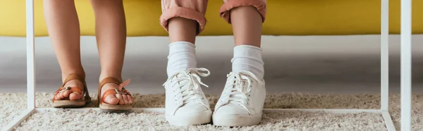 Vista recortada de la niñera en zapatillas de deporte y el niño en sandalias cerca de la alfombra en el suelo, imagen horizontal - foto de stock