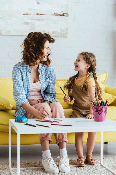 Niñera sonriente y niño feliz mirándose mientras dibujan juntos - foto de stock