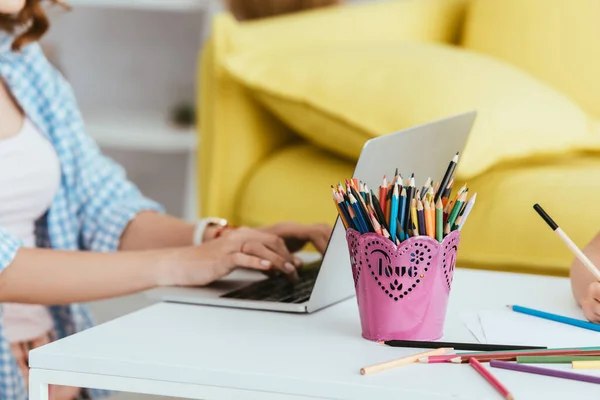 Vista ritagliata di freelance utilizzando il computer portatile sul tavolo vicino al portapenne con matite di colore e iscrizione amore — Foto stock