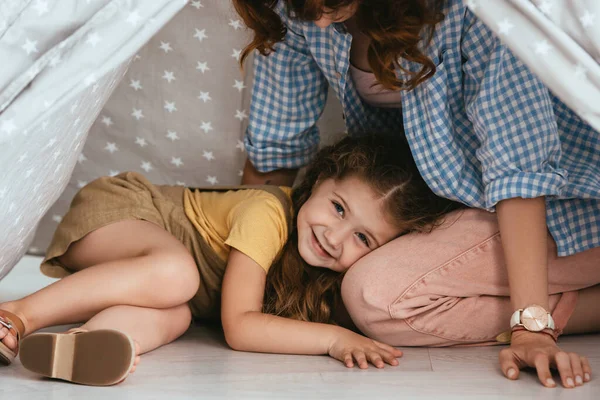 Cropped view of babysitter and happy child looking at camera from play tent — Stock Photo