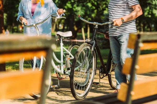 Concentration sélective du couple de personnes âgées marchant avec des vélos dans le parc — Photo de stock