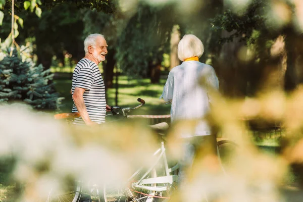 Foco seletivo de homem sorridente olhando para esposa perto de bicicletas no parque — Fotografia de Stock