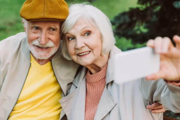 Focus sélectif de sourire couple âgé prenant selfie avec smartphone dans le parc — Photo de stock