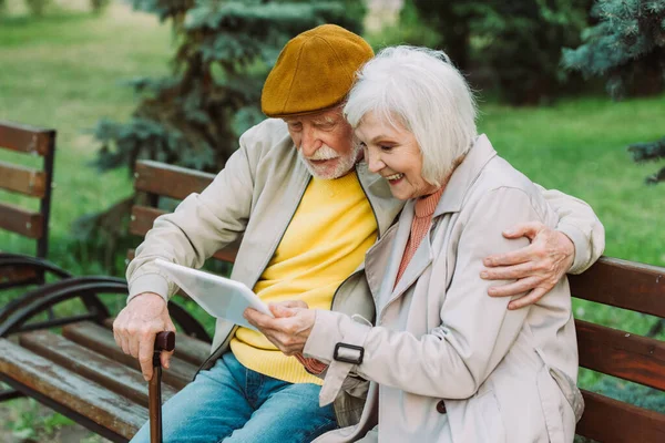 Positive Seniorin nutzt digitales Tablet neben Ehemann auf Parkbank — Stockfoto