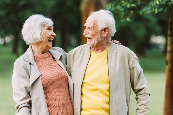 Веселая старшая пара улыбается друг другу, обнимаясь в парке — стоковое фото