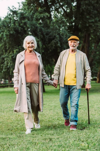 Senior woman smiling at camera while walking near husband in park — Stock Photo