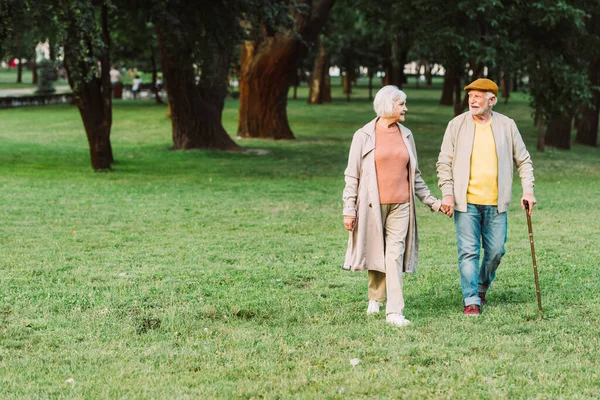 Улыбающаяся пожилая пара, держащаяся за руки во время прогулки в парке — стоковое фото