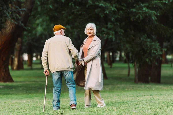 Donna anziana che guarda la fotocamera mentre cammina con il marito nel parco — Foto stock