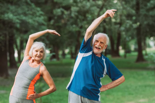 Fröhliches Senioren-Paar trainiert und blickt im Park in die Kamera — Stockfoto