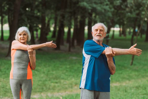 Селективное внимание пожилого мужчины, занимающегося спортом рядом с женой в парке — стоковое фото