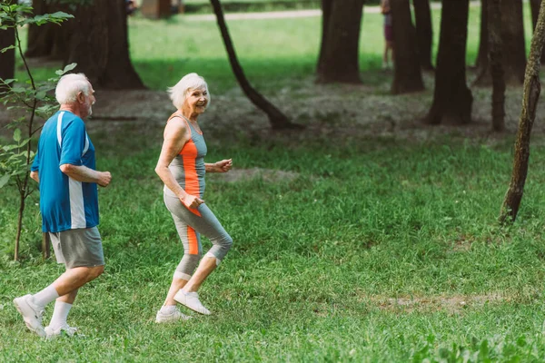 Усміхнена літня жінка біжить з чоловіком у парку — стокове фото
