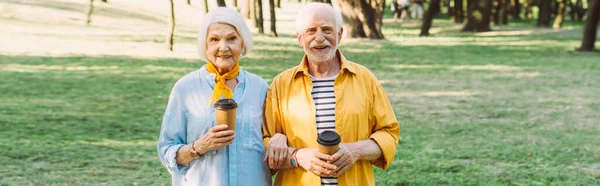 Coltivazione orizzontale di sorridente coppia anziana con caffè per andare a guardare la fotocamera nel parco — Foto stock
