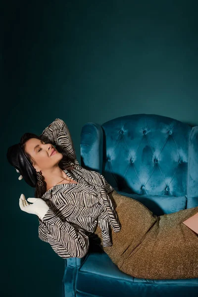 Pregnant woman in fashionable clothes lying on armchair with closed eyes on dark blue — Stock Photo