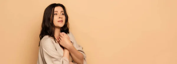 Website header of worried woman looking away while holding clenched hands near chest on beige — Stock Photo