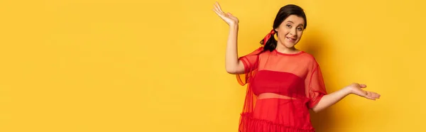 Panoramic shot of pregnant woman in red tunic standing with open arms while looking at camera on yellow — Stock Photo