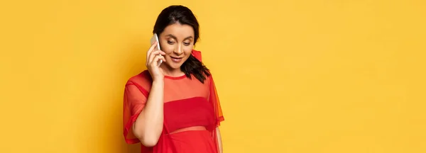 Panoramic shot of pregnant woman in red tunic talking on smartphone on yellow — Stock Photo