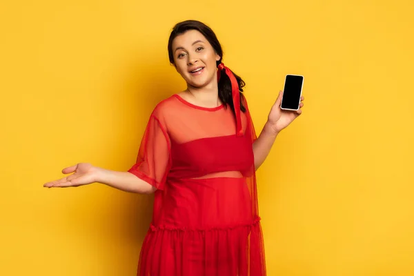 Вагітна жінка в червоному вбранні тримає смартфон з порожнім екраном в той час як стоїть жовтим — стокове фото