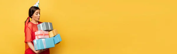 Panoramic shot of surprised pregnant woman in party cap holding gift boxes on yellow — Stock Photo