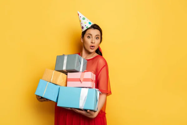 Pregnant woman in party car holding stack of gift boxes while looking at camera on yellow — Stock Photo