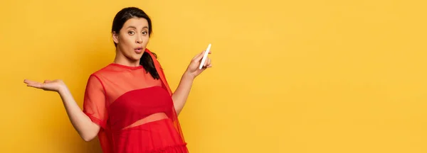 Horizontal image of confused pregnant woman showing shrug gesture while holding pregnancy test on yellow — Stock Photo